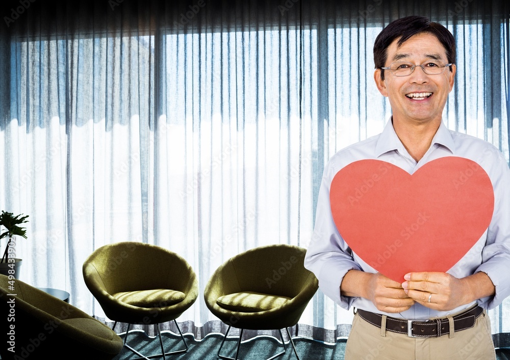 Portrait of asian man holding a heart shaped placard against living room in background