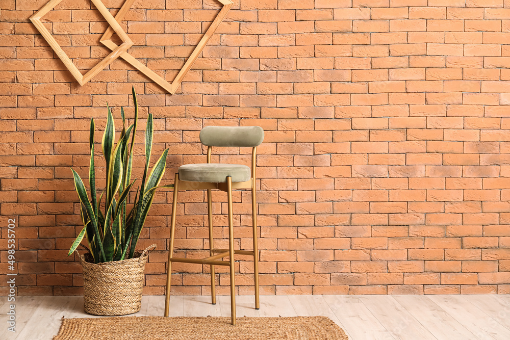 New chair with houseplant near brick wall