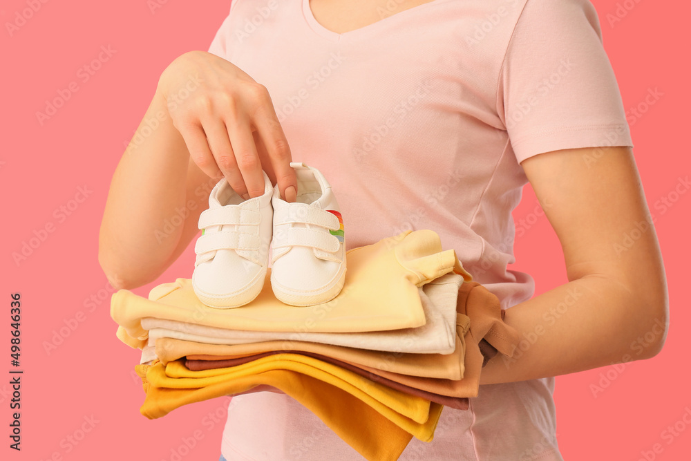 粉色背景下，一堆婴儿衣服和短靴的女人，特写