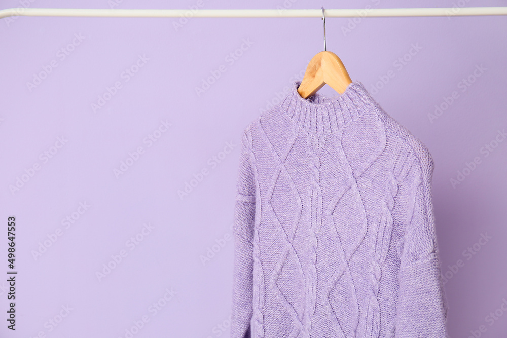 Rack with lilac sweater on color background