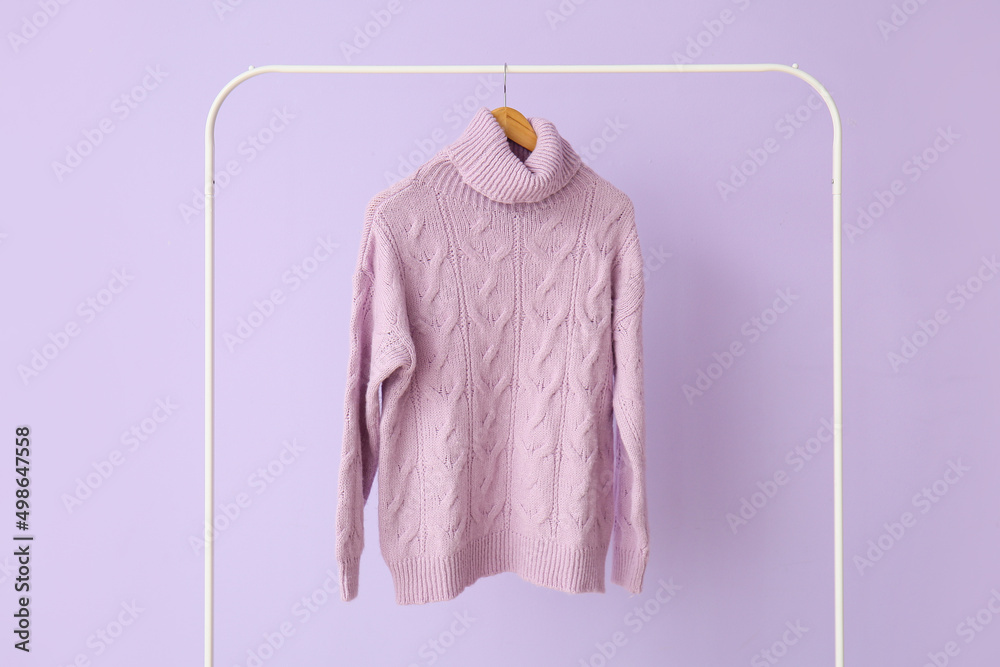 Rack with knitted sweater on lilac background