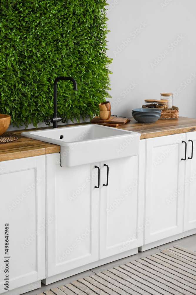 Sink, kitchen utensils and counters near light wall with decorative green grass