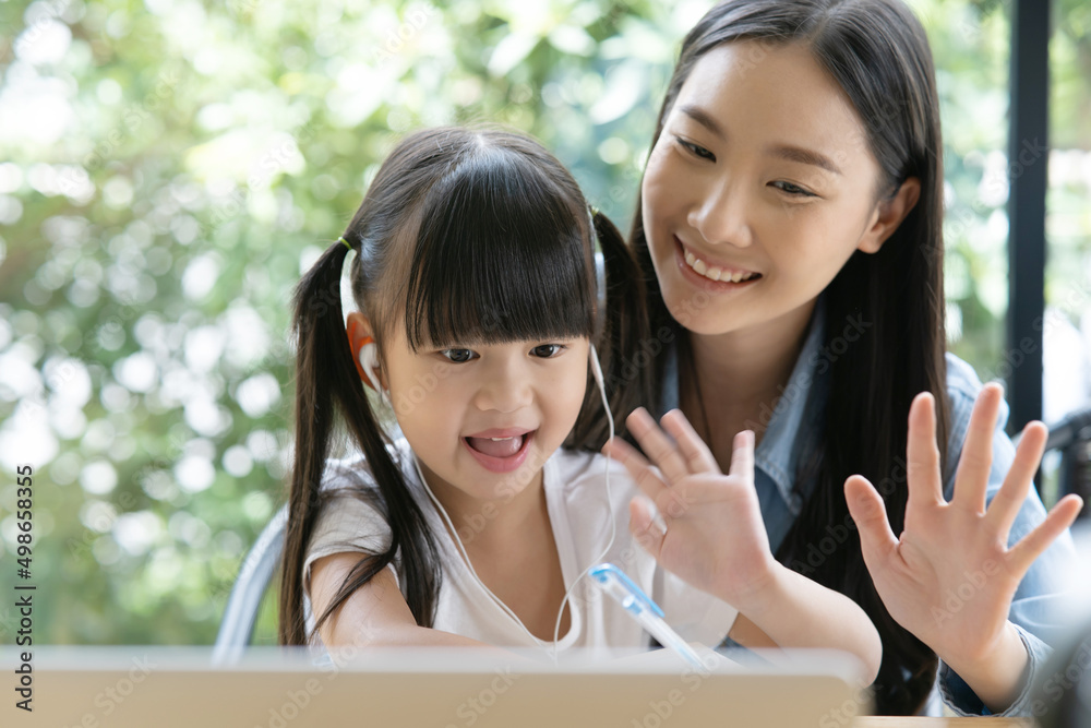 年轻的亚洲母亲在笔记本电脑上教女儿做家庭作业。亚洲小女孩喜欢学习