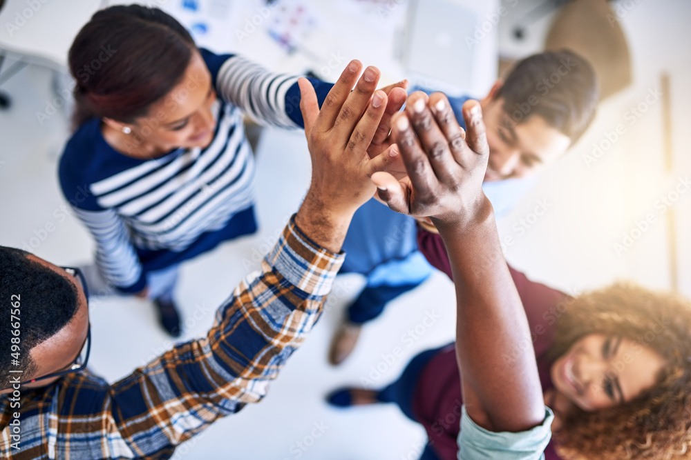 We can do this. High angle shot of a team of designers high fiving together in an office.