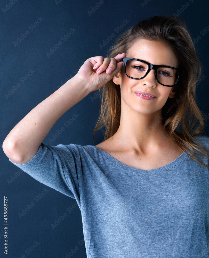 All the better to see with. Studio portrait of a cute teenage girl in glasses posing against a dark 