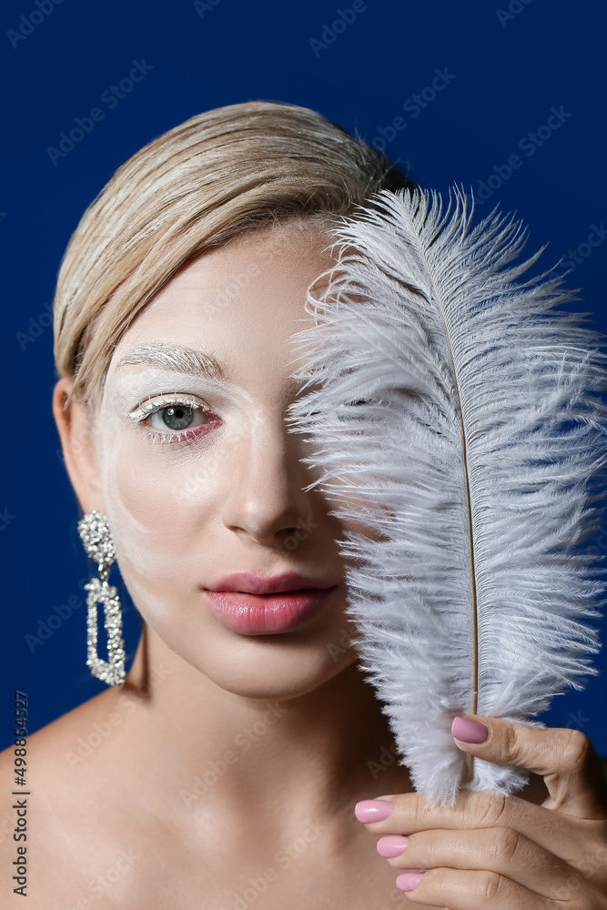 Beautiful young woman with creative makeup and feather on color background