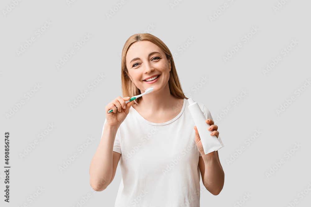 Beautiful mature woman brushing teeth on light background