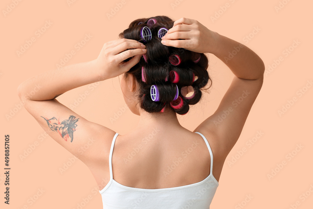 Beautiful young woman in hair rollers on color background, back view