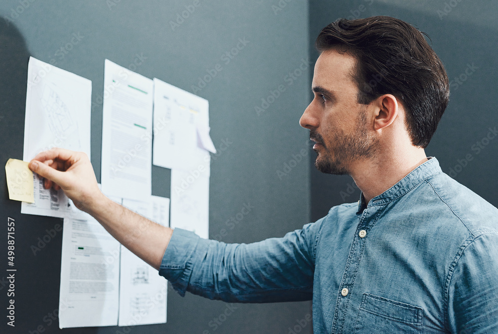 Whats next on his to-do list. Cropped shot of a handsome young businessman reading a sticky note whi