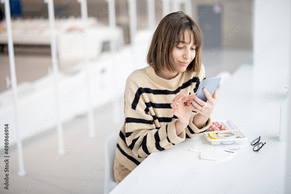 年轻女子坐在餐厅吃寿司卷时打电话。白人w