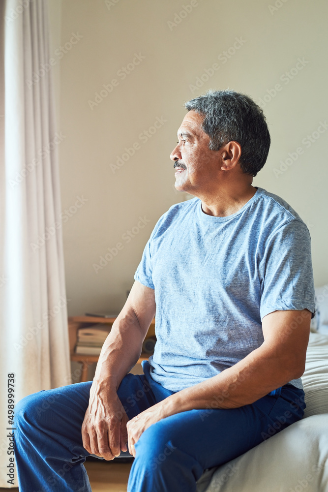 Today is going to be a great day. Shot of a confident mature man looking outside trough his window w