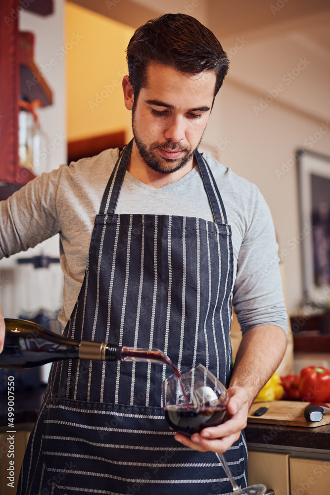 Improve your cooking - add wine. Shot of a happy young man pouring himself a glass of wine while coo