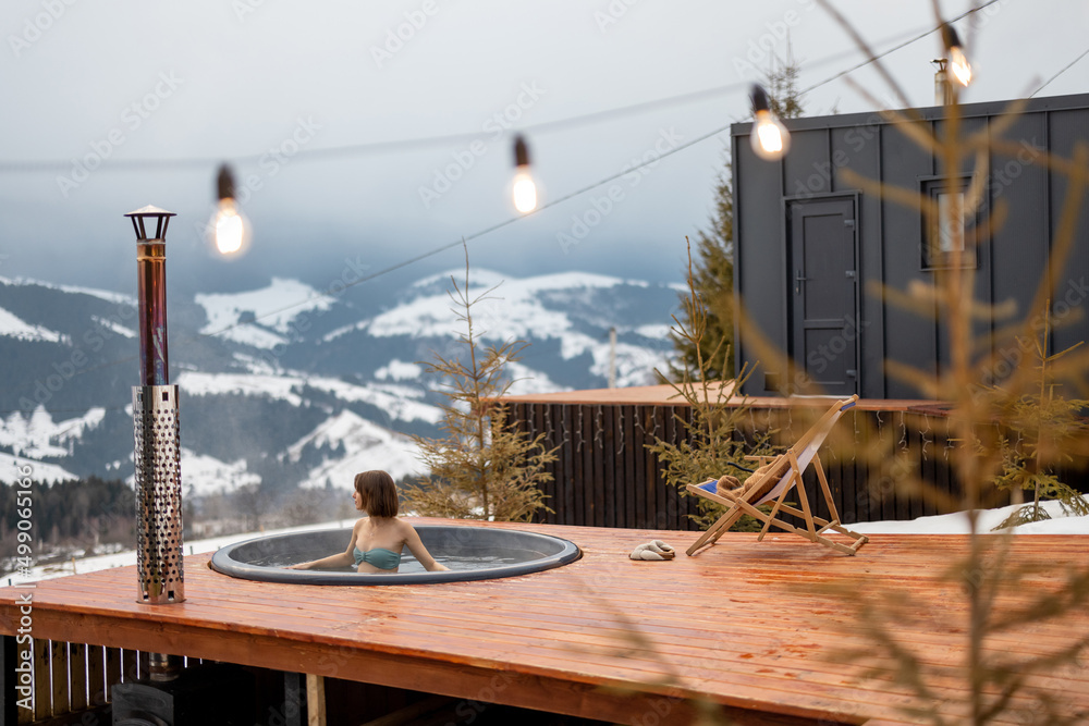 Woman swims in hot bath while resting at small modern house in the mountains on winter. Concept of r