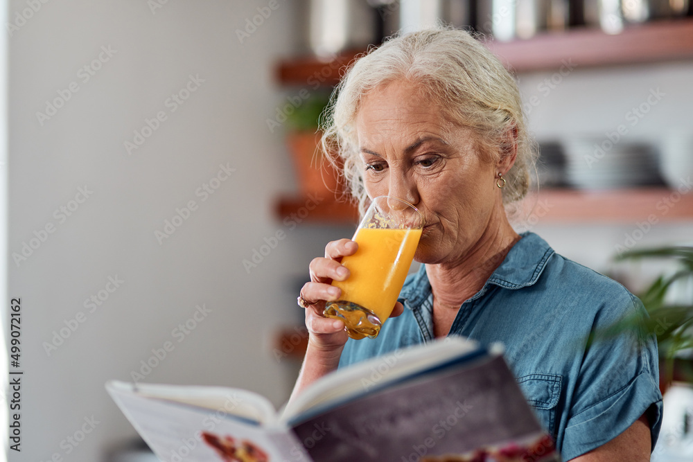 Its not a diet, its a way of life. Shot of a mature woman reading a book while having orange juice a