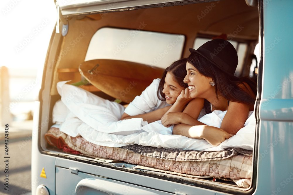 Anywhere is better together. Shot of two happy friends relaxing on a blanket in the true of their va