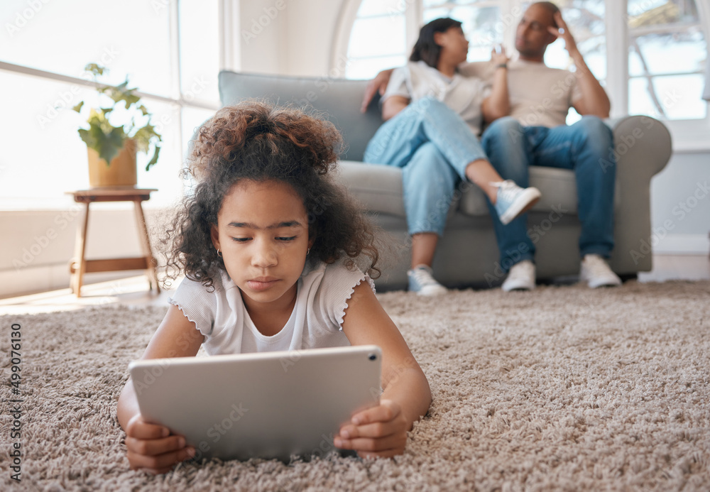 In her own little world. Shot of a little girl using a digital tablet while her parents relax.