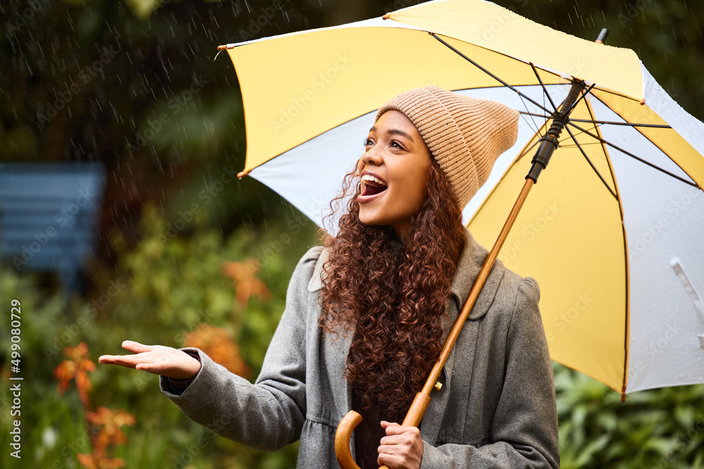 Making the best of a cold winters day. Shot of a young woman standing in the rain with an umbrella.