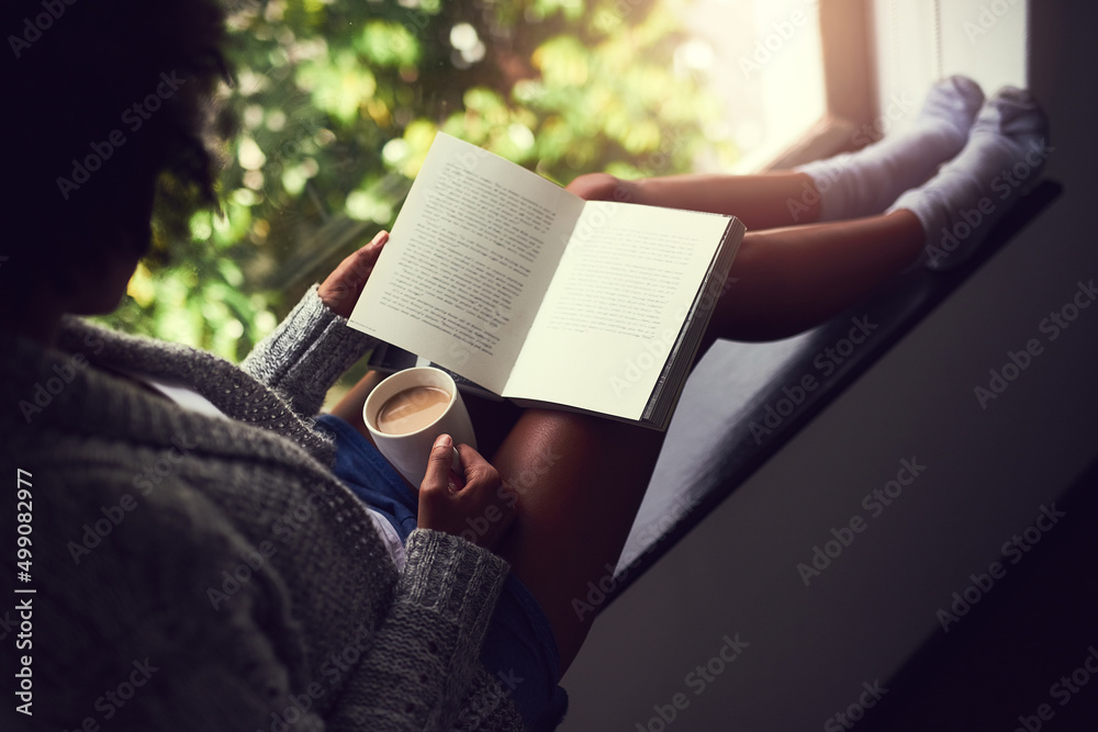 Escaping in the narrative. Shot of an unidentifiable young woman reading a book while enjoying a cup