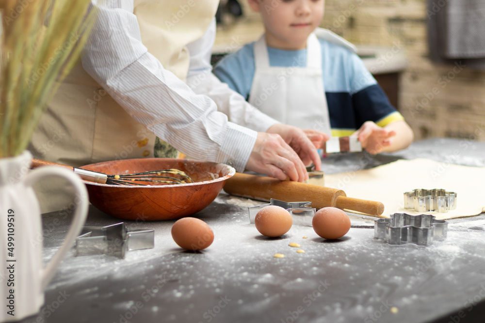 Mom and son are cutting out molds for baking sweet cookies from puff pastry on a black wooden table 