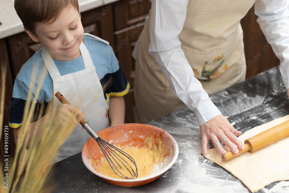 Mom and son in aprons roll out puff pastry for baking on a black kitchen table sprinkled with flour 