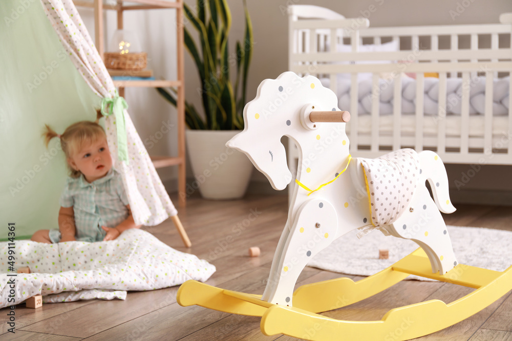 Classic rocking horse and adorable baby girl in playroom