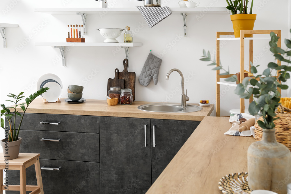 Wooden counters with sink and different cookware near white wall