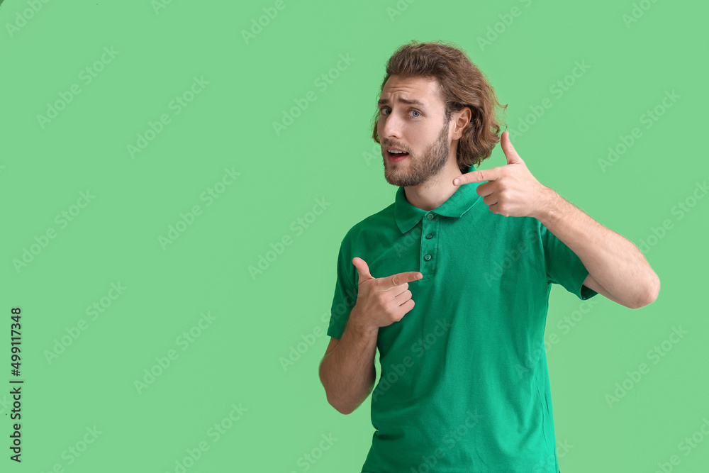 Handsome man in t-shirt pointing at something on green background