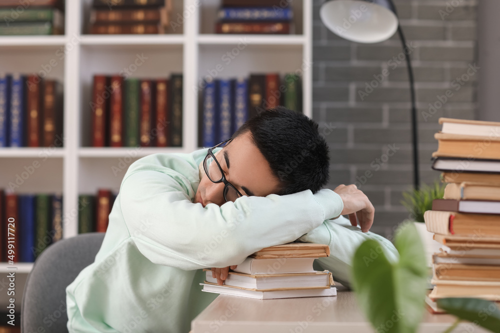 睡在图书馆桌子旁的亚洲男学生