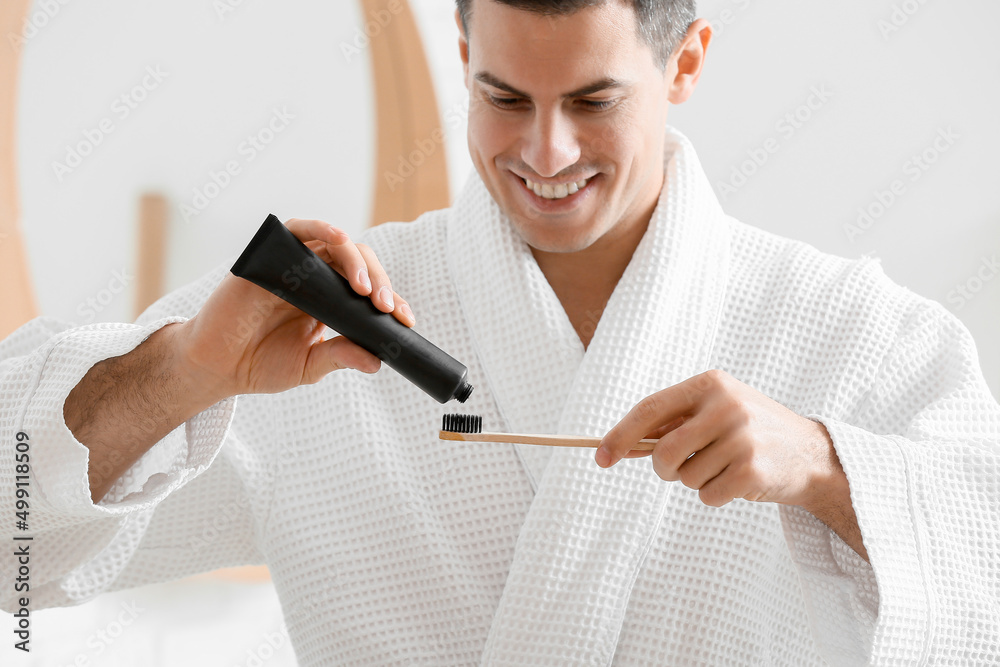 Handsome young man with activated charcoal tooth paste and brush in bathroom