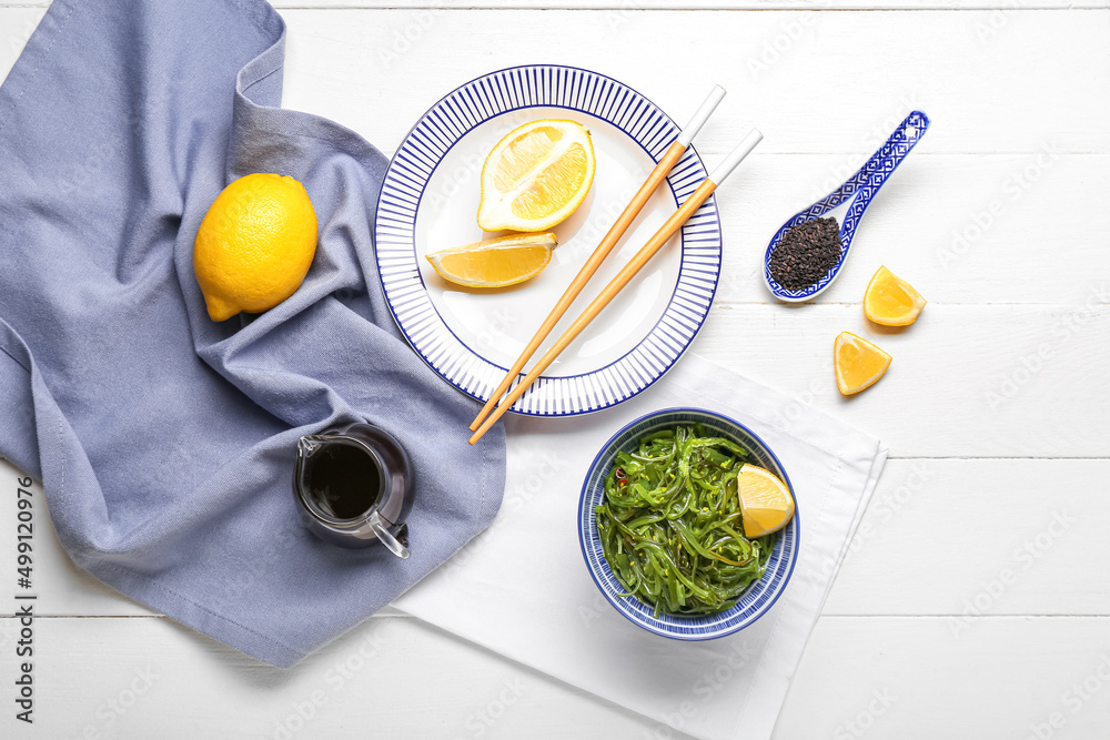 Bowl with healthy seaweed salad and ingredients on light wooden background