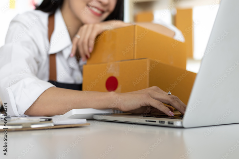 Small start-up business owners work with laptops in warehouses. A woman checks online orders in prep