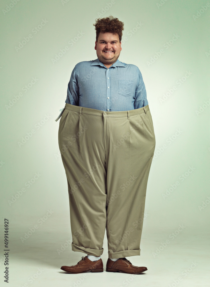 Diet progress. Shot of an overweight man wearing a pair of oversized pants looking pleased.