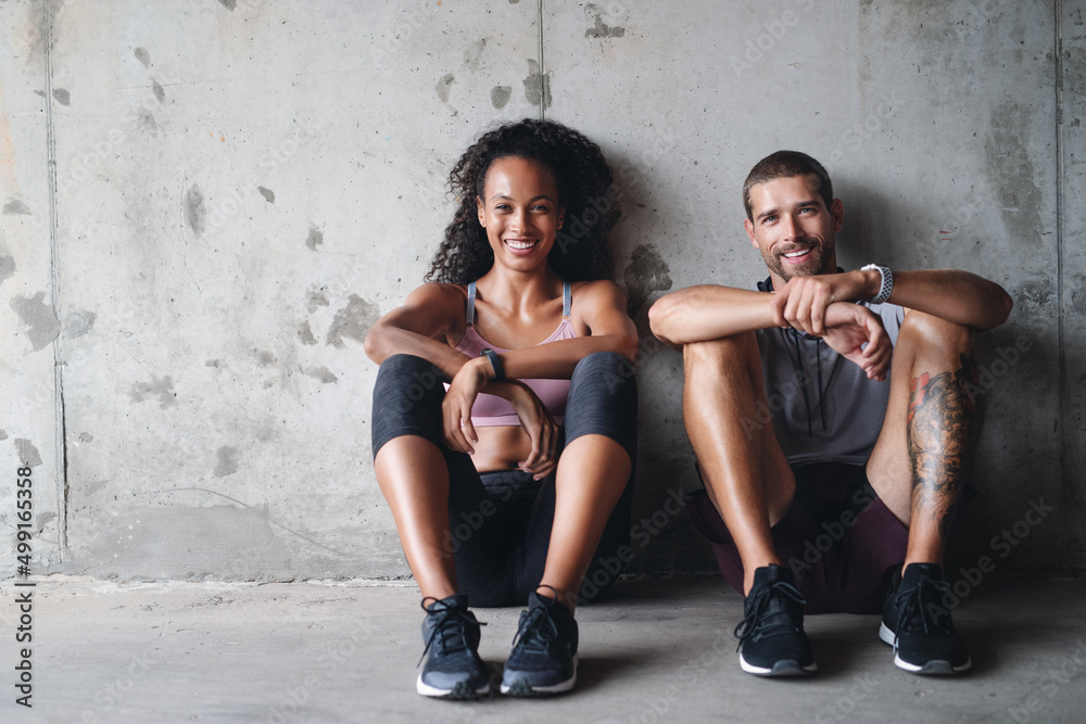 Were down but not out. Portrait of a sporty young couple sitting down against a wall while exercisin