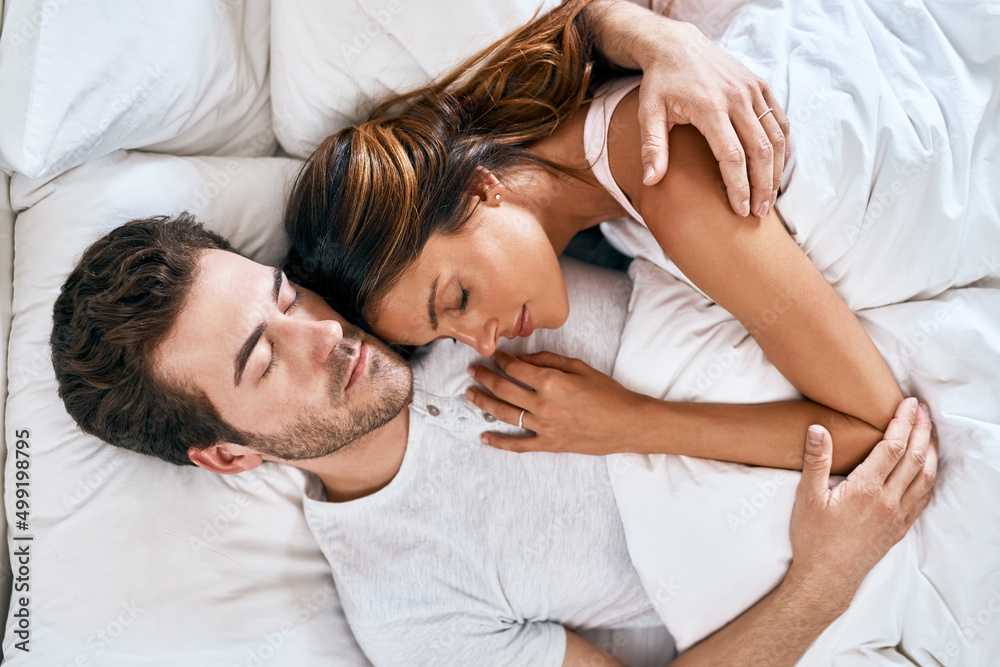 Comfort is love. High angle shot of a loving young couple sleeping together at home.