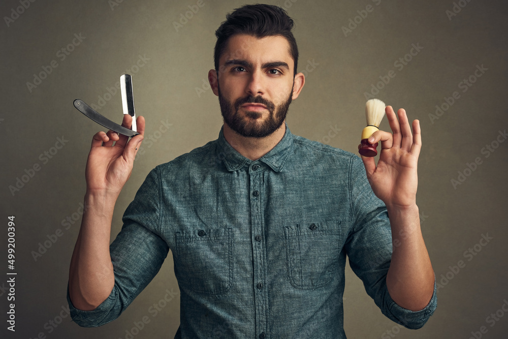 胡子正在建造中。一个英俊的年轻人拿着一把直剃刀刮胡子的工作室镜头