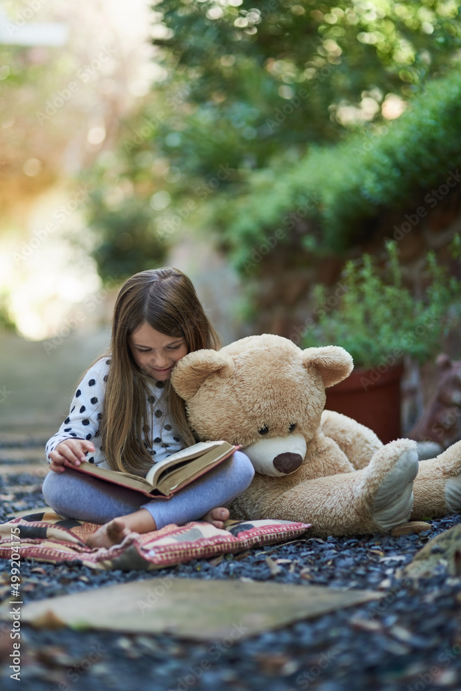 Teddy seems to be taking a nap from storytime. Shot of a little girl reading a book with her teddy b