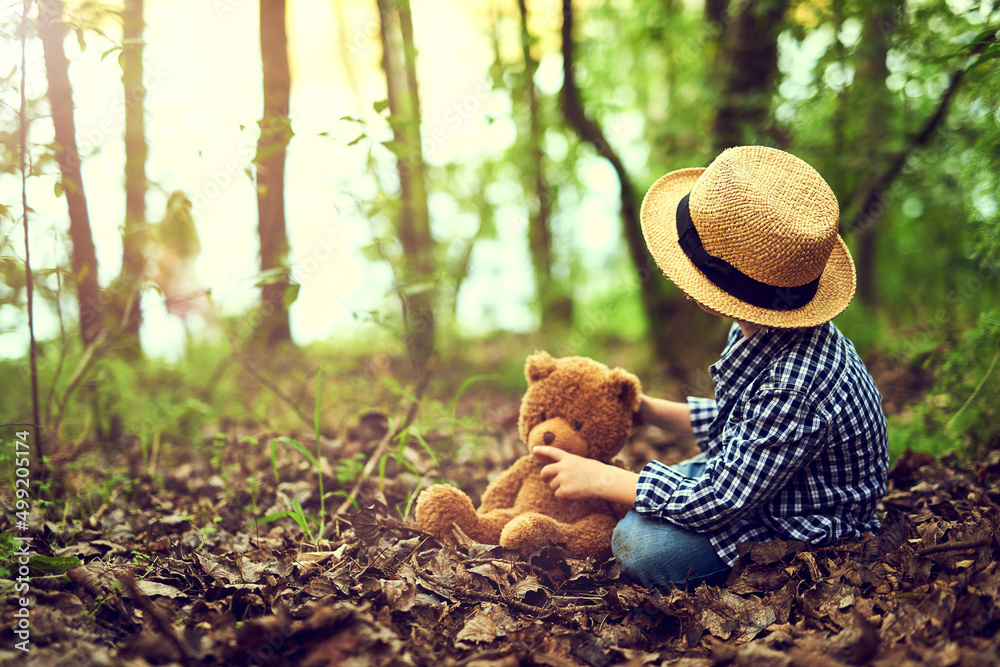 Shh Teddy, I heard something. Shot of a little boy sitting in the forest with his teddy bear.