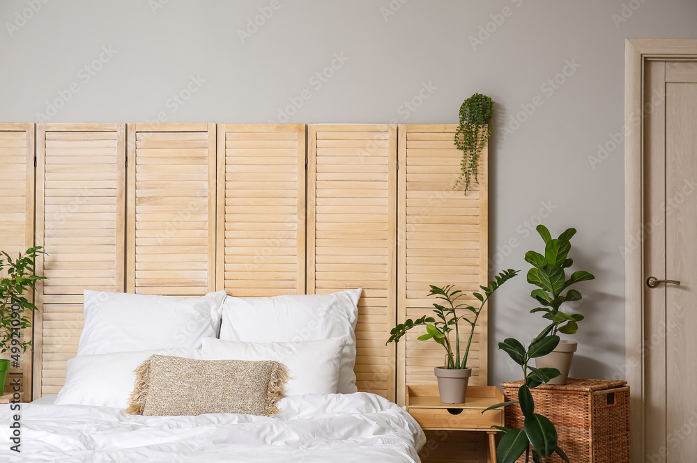 Interior of light bedroom with houseplants and folding screen