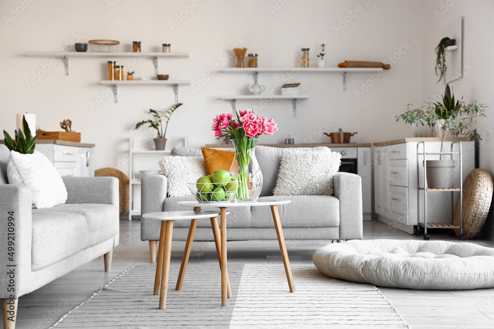 Basket with fresh apples and vase with tulips on table in stylish room interior