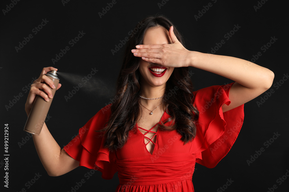 Beautiful young woman with hair spray on black background