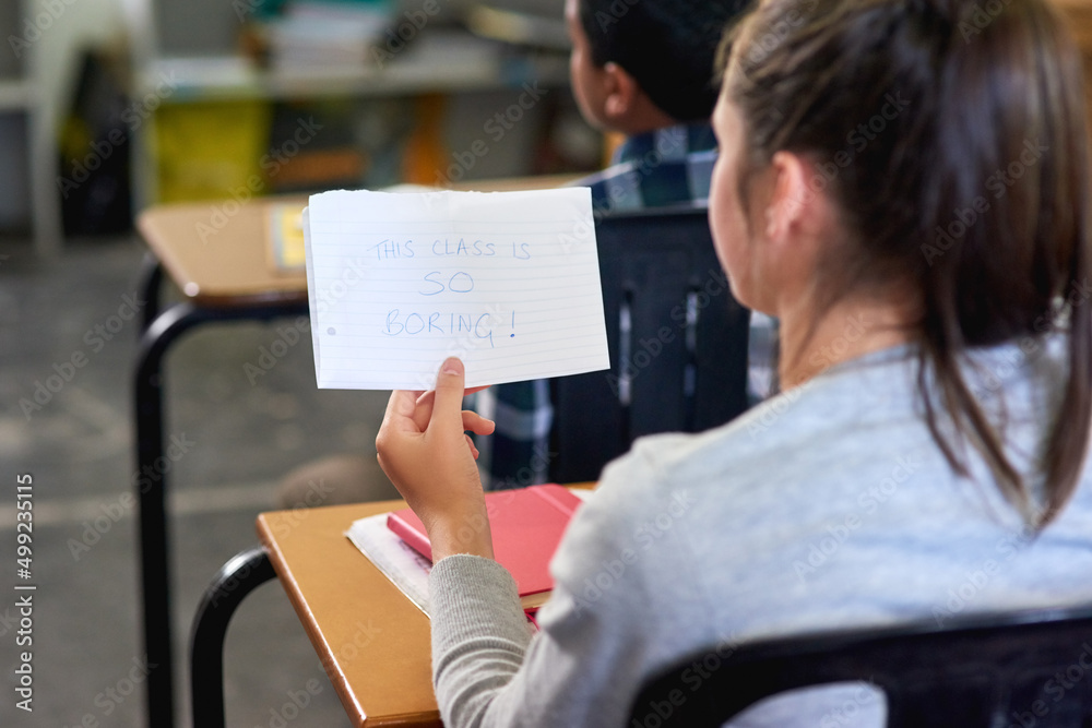 Tell me something I dont know. Rearview shot of an unidentifiable schoolgirl reading a note in class