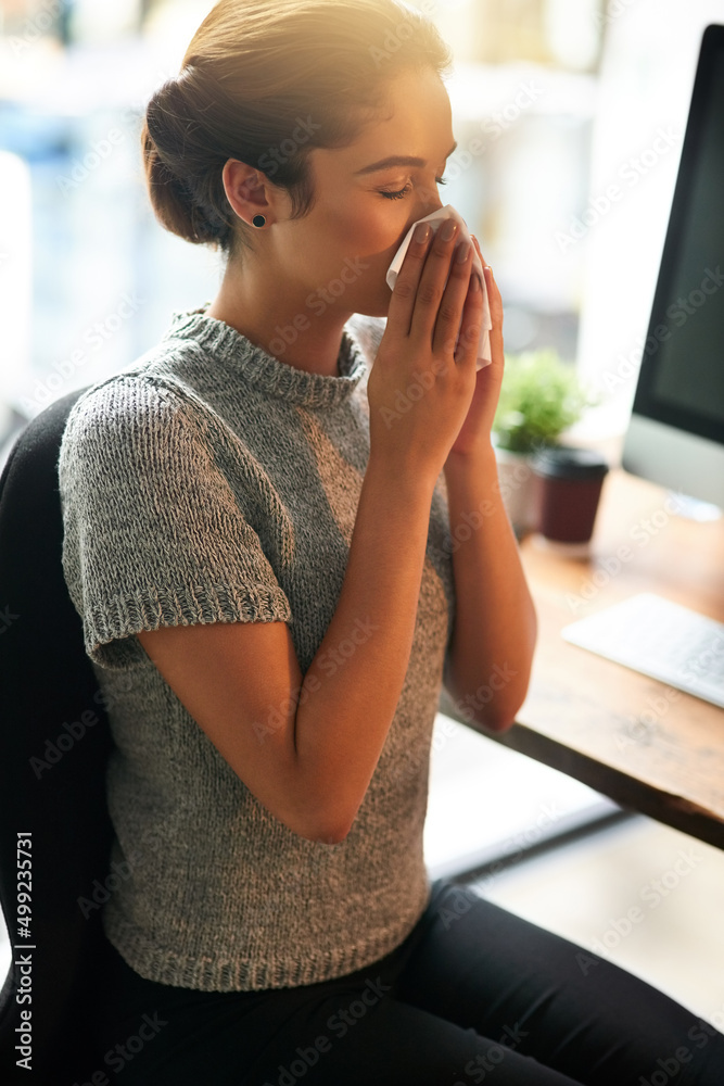 Its that time of the year. Shot of a young businesswoman blowing her nose in an office.