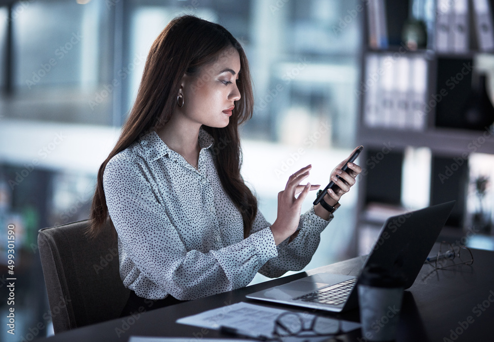 Sometimes success requires a bit of extra time. Shot of a young businesswoman using a cellphone whil