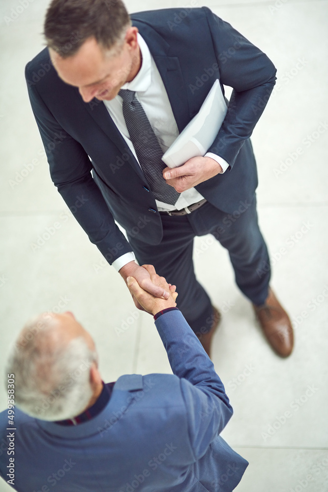 Striking yet another deal. High angle shot of two businessmen shaking hands in an office.