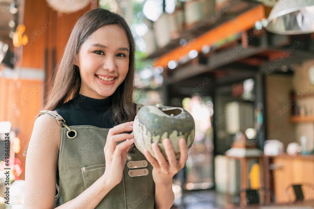 亚洲女性成年陶艺家设计师手持陶瓷粘土花瓶，用欢快的骄傲微笑手工制作