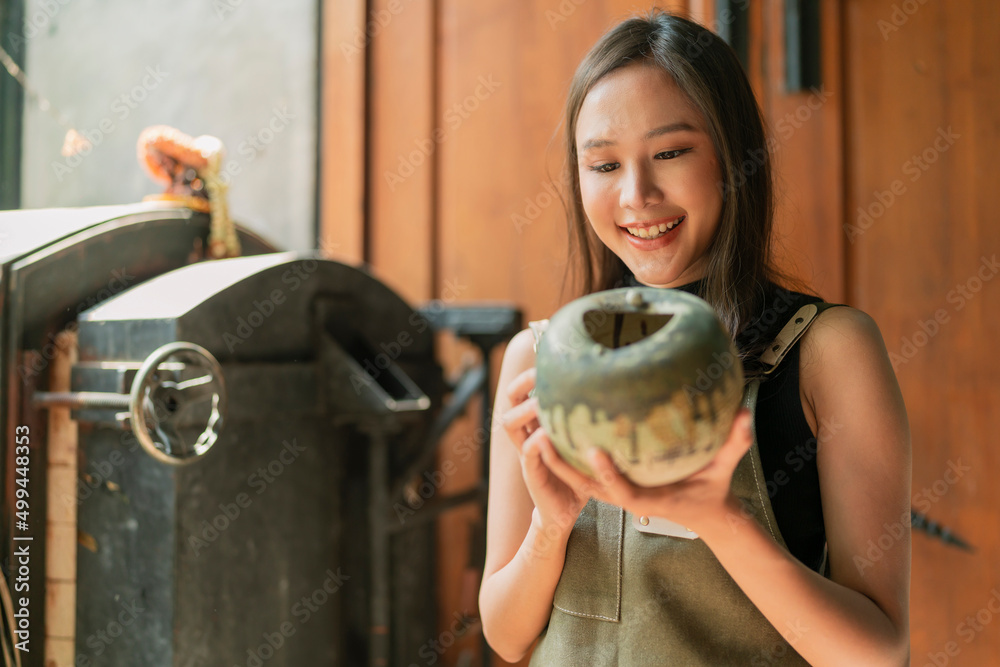 亚洲女性成年陶艺家设计师手持陶瓷粘土花瓶，用欢快的骄傲微笑手工制作