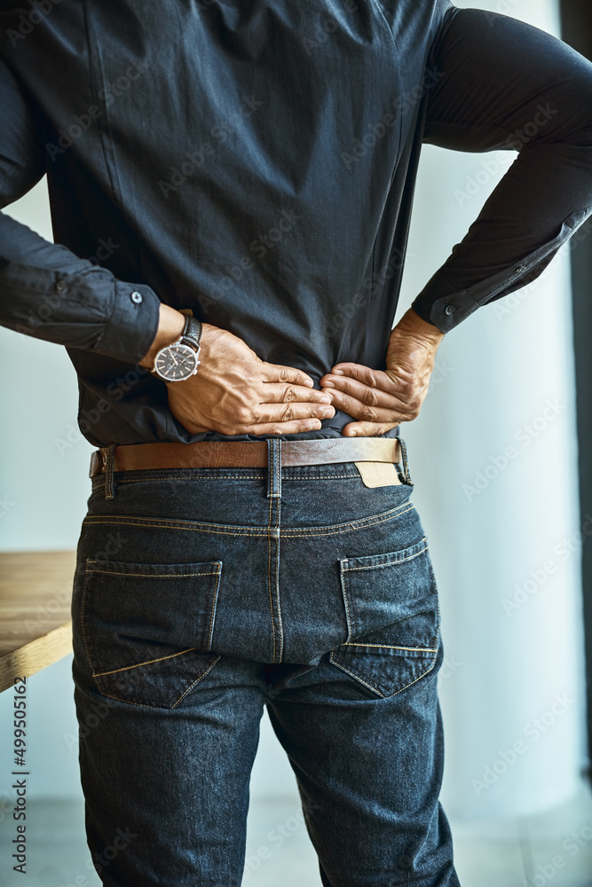 His back muscles are getting tense and tight. Shot of a young businessman suffering from back pain w