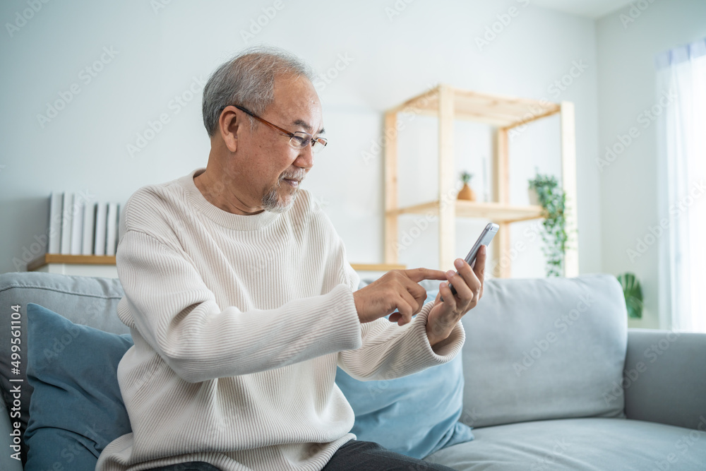 Asian senior elderly male using mobile phone in living room at home. 