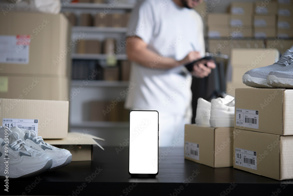 Smartphone with blank white screen standing on the desktop in the warehouses. Asian man online selle