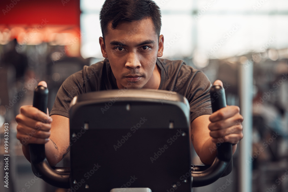 Ridding my way to some tight calves. Shot of a young man using an exercise bike in the gym.